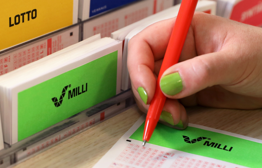 Kuvassa pelaaja täyttää Milli-peli kuponkia Veikkauksen myyntipisteellä. Taustalla näkyy Lotto-kuponki.