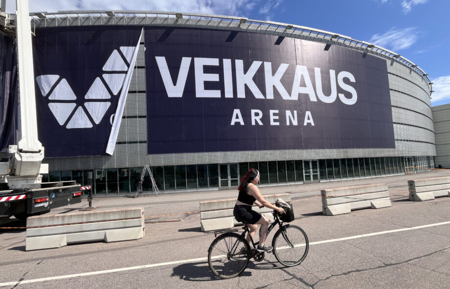 Kuvassa Veikkaus Arena Helsingissä. Veikkauksen mainoskylttiä vielä asennetaan. Etualalla pyöräilijä.