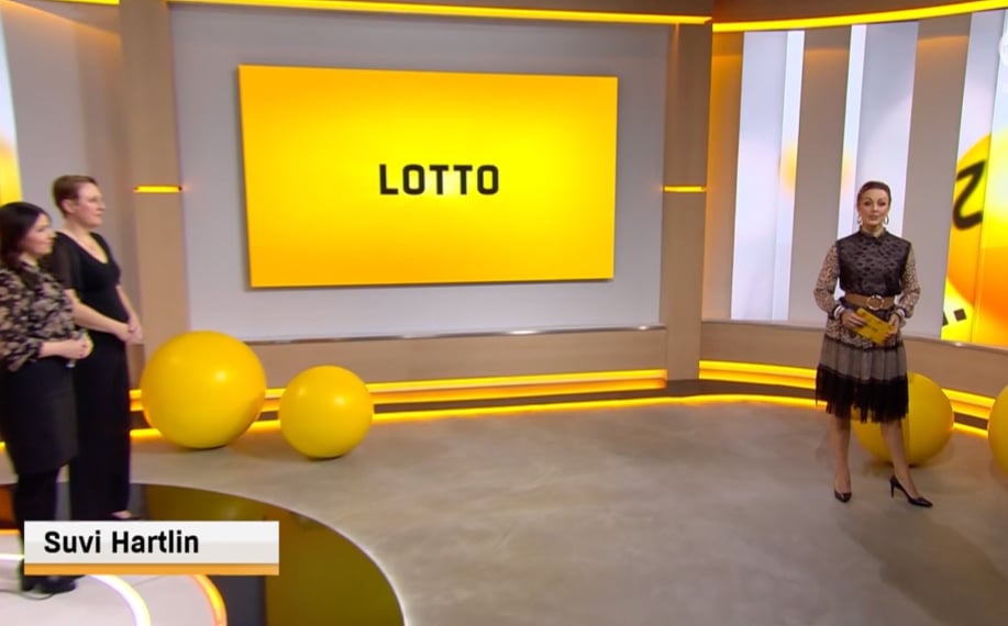 Kuvassa Lotto-lähetys ja juontaja Suvi Hartlin suomalaiselta näyttävässä mekossa. Taustalla näkyvässä TV-ruudussa "Lotto" -logo.