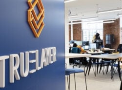 Oranssi-valkoinen Truelayer logo toimiston taivaan sinisellä seinällä