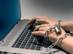 Kädet kahlittu ketjuihin kirjoittamalla kannettavan näppäimistö. Kuvaa haitallista rahapelaamista.